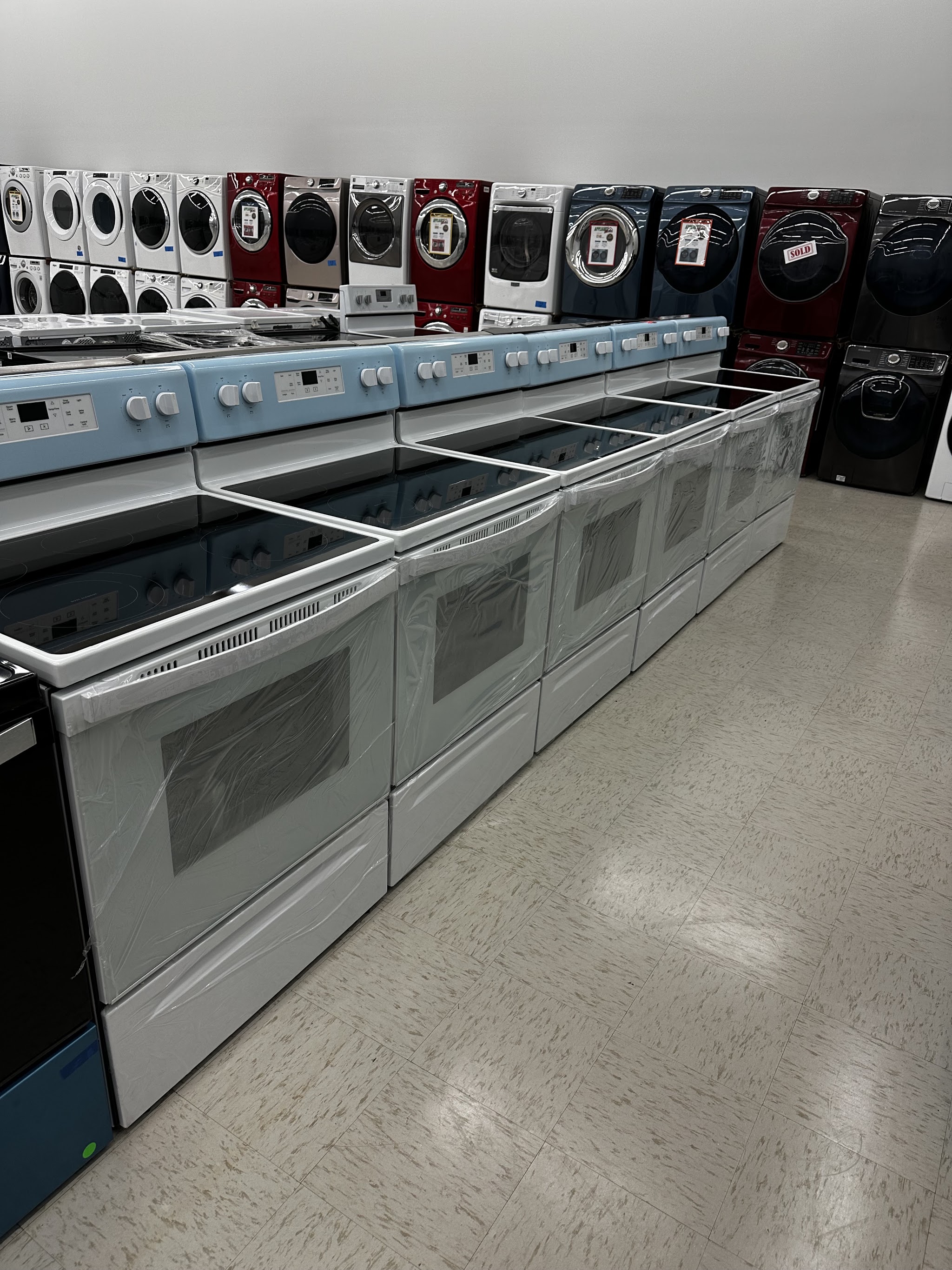 A row of electric ranges with washers and dryers behind them